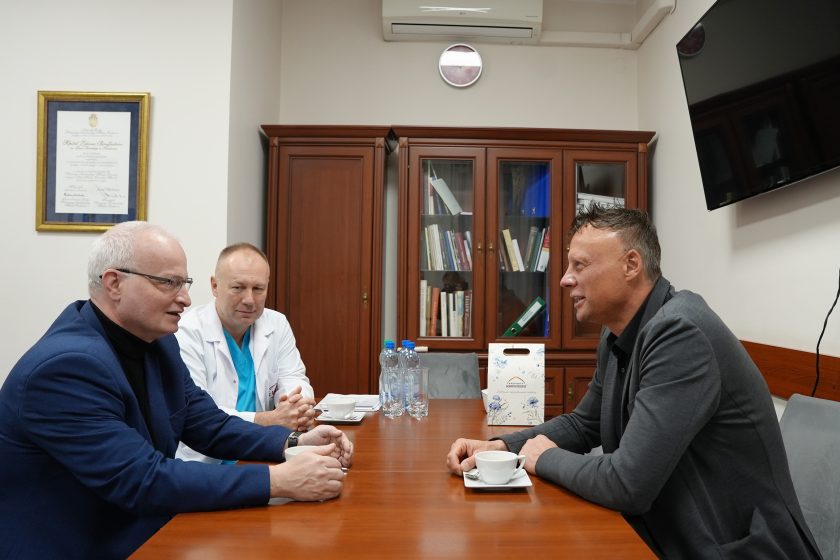 Uczestnicy spotkania podczas rozmowy w gabinecie administracyjnym. Na stole przygotowano poczęstunek i dokumenty, a w tle widoczne są szafy z literaturą specjalistyczną