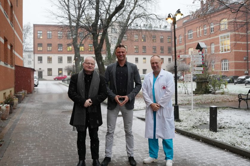 Przedstawiciele szpitala podczas krótkiego spaceru po terenie placówki w zimowej scenerii. W tle widoczne są zabytkowe budynki i alejki ogrodowe pokryte świeżym śniegiem