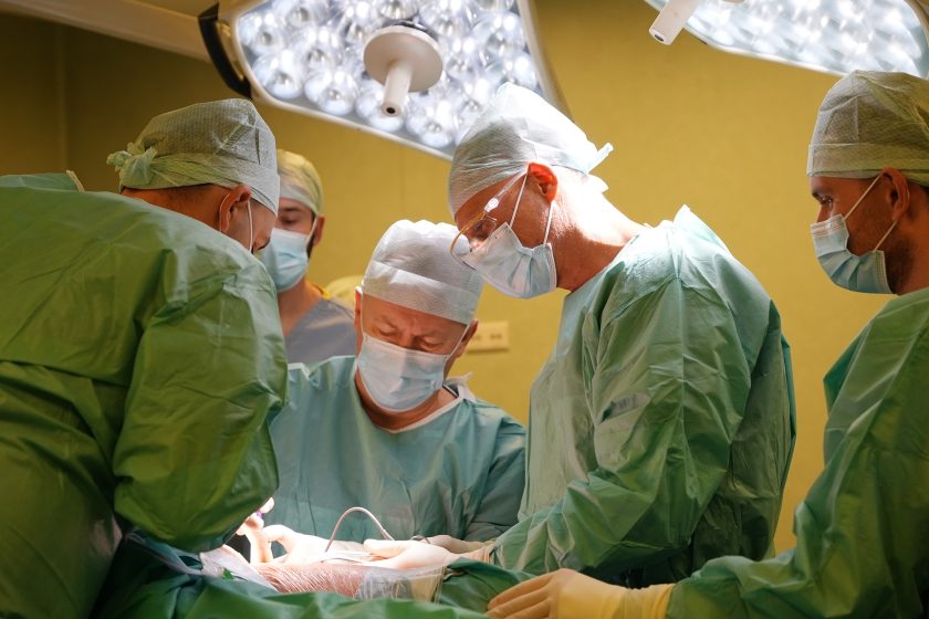 Chirurdzy wykonują skomplikowany zabieg w sali operacyjnej. Personel w pełnym zabezpieczeniu aseptycznym koncentruje się na precyzyjnych czynnościach