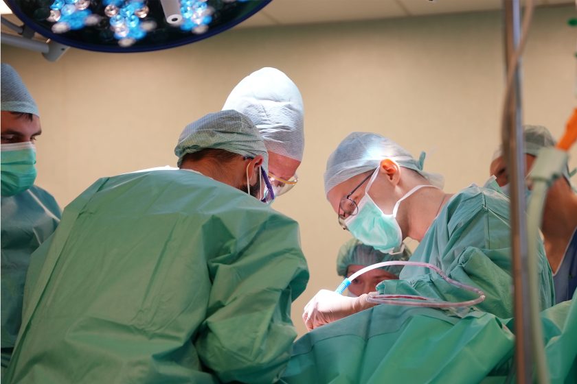 Fragment trwającej operacji, w której uczestniczy kilku specjalistów. Personel medyczny pracuje przy pacjencie, korzystając z nowoczesnego oświetlenia i sprzętu chirurgicznego