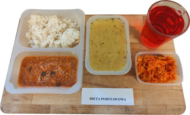 Zestaw obiadowy w diecie podstawowej: zupa jarzynowa z makaronem, ryż z gulaszem, surówka z marchewki i jabłka oraz napój owocowy. Posiłek podany w plastikowych pojemnikach na drewnianej desce