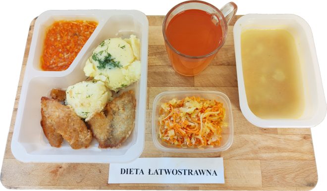 „Zestaw obiadowy w diecie łatwostrawnej w jednorazowym pojemniku: zupa krem w osobnym opakowaniu, kawałki panierowanego mięsa, ziemniaki z koperkiem, surówka z marchewki i kapusty oraz sos w osobnej przegródce. Obok szklanka herbaty