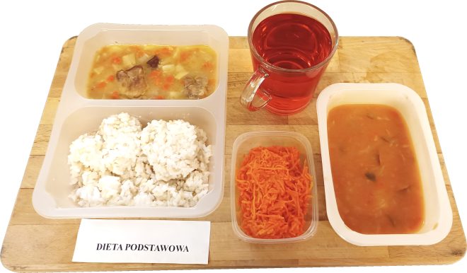 Obiad podany w pojemnikach: gulasz z warzywami, porcja białego ryżu, surówka z tartej marchewki oraz zupa w osobnym pojemniku. Do zestawu dołączona jest szklanka czerwonego kompotu. Przed zestawem znajduje się kartka z napisem „Dieta podstawowa”