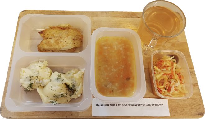 Zestaw obiadowy w diecie z ograniczeniem łatwo przyswajalnych węglowodanów. Na tacy znajduje się porcja gotowanych ziemniaków z koperkiem, filet drobiowy smażony na złoto, miska lekkiej zupy jarzynowej oraz mała porcja surówki z białej kapusty i marchewki. Do posiłku podano również szklankę herbaty. Przed tacą widoczna kartka z opisem diety