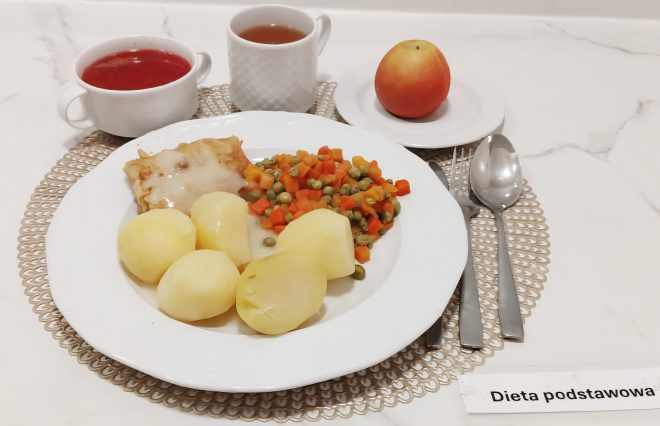 Obiad w diecie podstawowej to połączenie delikatnych i lekkostrawnych składników. Serwujemy gotowane ziemniaki, rybę w łagodnej panierce z sosem oraz klasyczną marchewkę z groszkiem. Do zestawu podawany jest kompot, herbata oraz owoc, który uzupełnia posiłek o naturalne witaminy