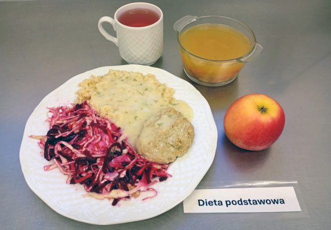 „Porcja obiadowa w diecie podstawowej – kotlet mielony z sosem koperkowym, kasza, surówka z czerwonej kapusty i buraków. Do posiłku podano kompot owocowy, herbatę i jabłko.