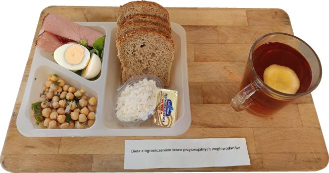 Śniadanie w diecie z ograniczeniem łatwo przyswajalnych węglowodanów: pełnoziarniste pieczywo, jajko na twardo, plasterki wędliny, twarożek, masło, sałatka z ciecierzycy oraz herbata z cytryną