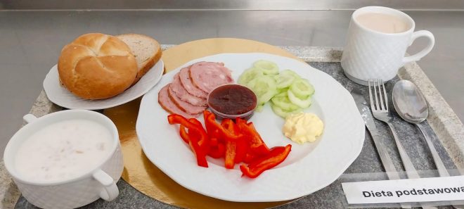 Śniadanie na diecie podstawowej: pieczywo pszenne i żytnie, płatki owsiane na mleku, wędliny, pokrojona papryka i ogórek, dżem oraz masło; do picia kawa z mlekiem