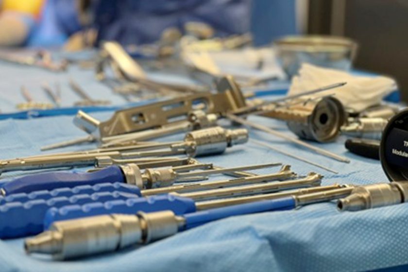 Zbliżenie na stół operacyjny pokryty niebieską serwetą, na którym ułożone są liczne narzędzia chirurgiczne, w tym wiertła, uchwyty i metalowe elementy zestawu operacyjnego