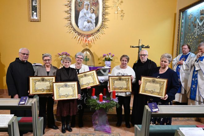 Siedmioosobowa grupa stoi przed ołtarzem kaplicy, każda z kobiet trzyma duży oprawiony dyplom. Po bokach stoją dwaj zakonnicy. Za nimi widoczny jest obraz Maryi z Dzieciątkiem, ołtarz i kapłani w białych ornatach