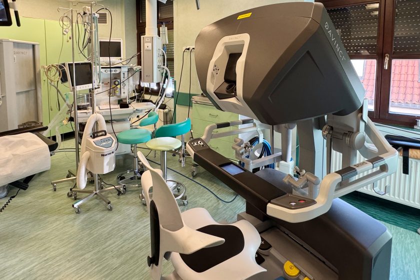 Widok sali operacyjnej z pełnym stanowiskiem robota da Vinci: konsolą operatorską, systemem wizyjnym oraz elementami wyposażenia sali zabiegowej. Na pierwszym planie znajduje się ergonomiczne stanowisko chirurga z podłokietnikami i wizjerem stereoskopowym