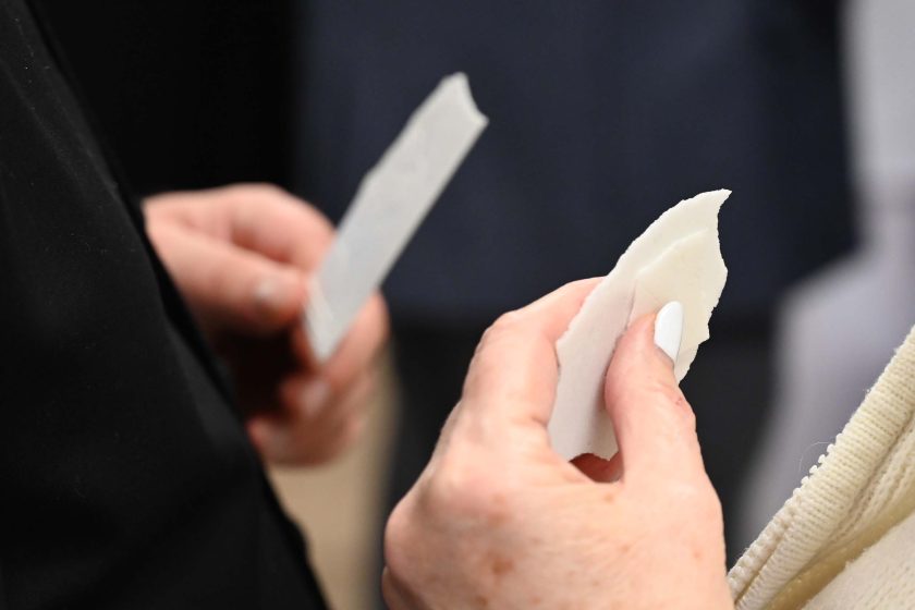 Zbliżenie na dłonie podczas łamania się opłatkiem – kobieca dłoń z białym manikiurem trzyma ułamany kawałek opłatka, w tle rozmyta sylwetka drugiej osoby z opłatkiem w ręku