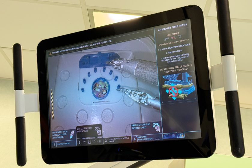 Monitor systemu da Vinci prezentujący obraz z kamery endoskopowej podczas ćwiczeń na trenażerze. Na ekranie widoczne są narzędzia robota wykonujące precyzyjne manewry oraz panel z instrukcjami dotyczącymi pracy ramion i konfiguracji stołu operacyjnego