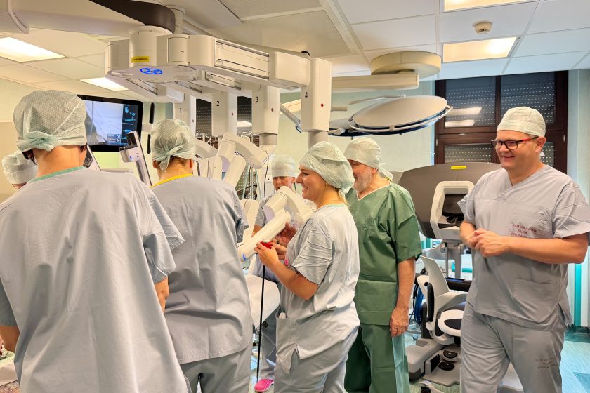 Personel bloku operacyjnego w trakcie praktycznych ćwiczeń z obsługi robota da Vinci. Uczestnicy stoją wokół stołu operacyjnego i ramion robota, wymieniając się uwagami i obserwując przebieg zadania treningowego. Atmosfera skupienia i współpracy