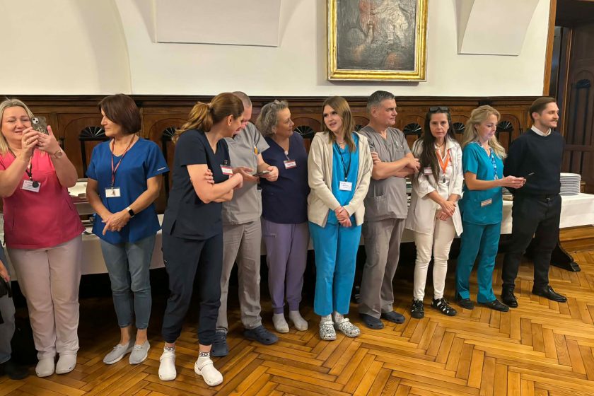 Pracownicy szpitala stojący w rzędzie podczas spotkania opłatkowego, w tle stoły z poczęstunkiem