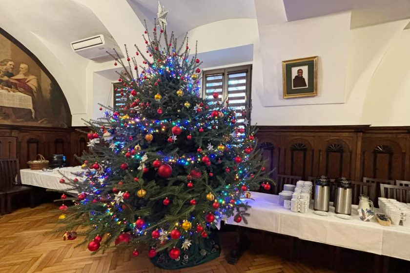 Choinka bożonarodzeniowa ozdobiona kolorowymi bombkami i światełkami, stojąca w zabytkowej sali szpitala.