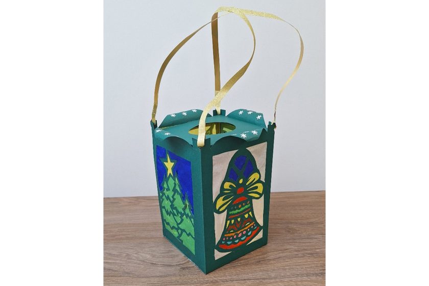 Zielony kartonowy lampion z uchwytami ze złotej wstążki, ozdobiony motywami choinki i dzwonka