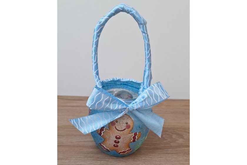 Mały lampion w formie koszyczka z uchwytem, ozdobiony niebieską kokardą i motywem piernikowego ludzika