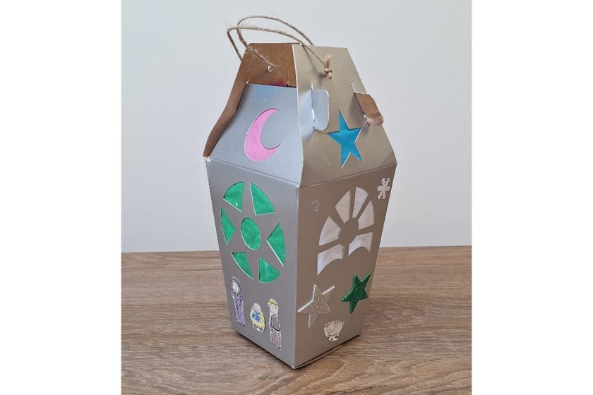 Ręcznie wykonany kartonowy lampion w kształcie domu, ozdobiony kolorowymi gwiazdami, księżycem i wyciętymi okienkami, z uchwytem ze sznurka
