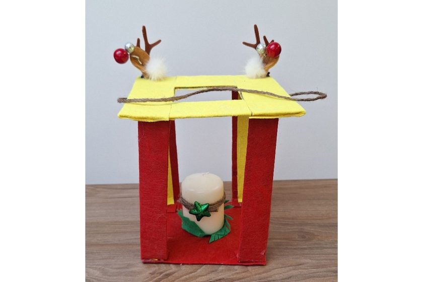 Ręcznie wykonany lampion z filcu w kolorach czerwonym i żółtym, z czterema filcowymi kolumnami i świeczką w środku, ozdobiony motywami świątecznymi