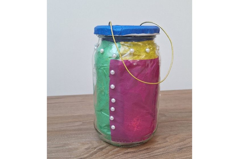 Szklany słoik ozdobiony kolorową bibułą w odcieniach zieleni, różu i żółci, z perełkami i zawieszką ze złotego sznurka