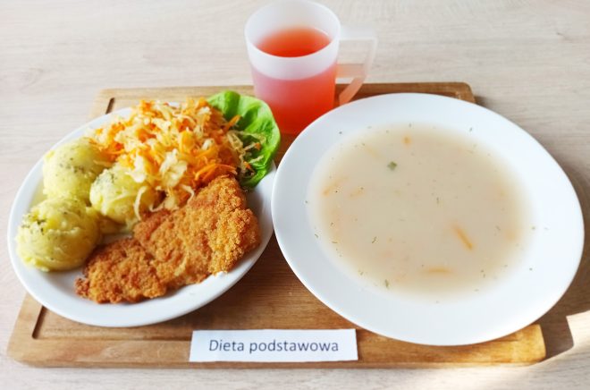 Obiad w diecie podstawowej: zupa jarzynowa, panierowany kotlet, gotowane ziemniaki, surówka z kiszonej kapusty i marchwi oraz kompot, podane na tacy