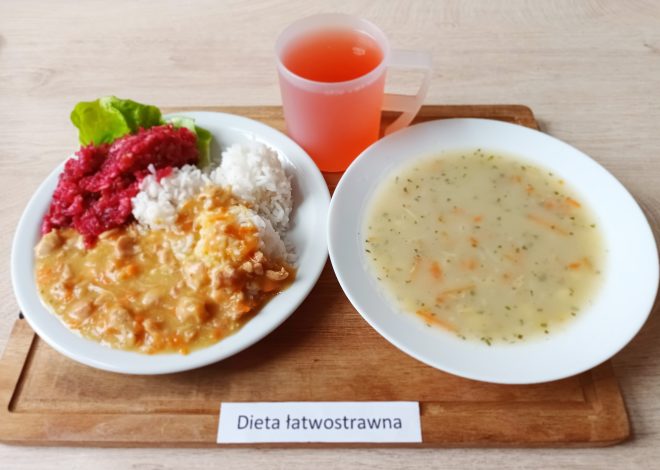 Obiad w diecie łatwostrawnej: talerz z porcją białego ryżu, gotowanym mięsem w jasnym sosie oraz buraczkami, obok talerz z lekką zupą jarzynową i kubek czerwonego napoju, posiłek podany na drewnianej tacce