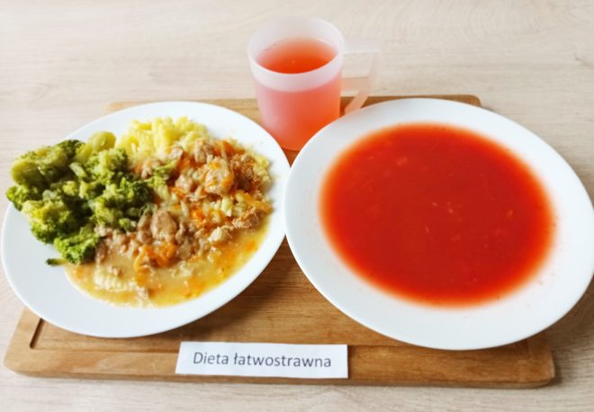 Obiad w diecie łatwostrawnej: zupa pomidorowa, drugie danie z gotowanymi brokułami, ryżem i mięsem w sosie oraz napój owocowy, podane na tacy