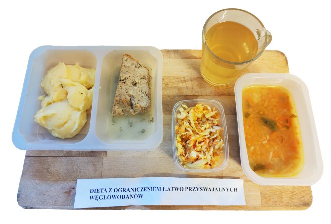 Obiad w diecie z ograniczeniem łatwo przyswajalnych węglowodanów: puree ziemniaczane, porcja mięsa w sosie koperkowym, surówka z kapusty, zupa jarzynowa oraz herbata, podane w pojemnikach na drewnianej desce