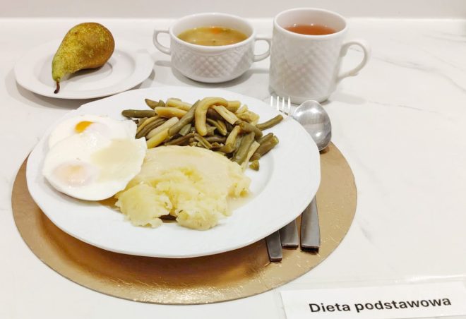 Obiad w diecie podstawowej: jajka sadzone, puree ziemniaczane oraz fasolka szparagowa, podane na talerzu; obok gruszka, zupa oraz herbata