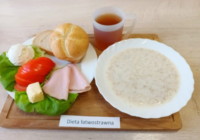 Śniadanie w diecie łatwostrawnej: bułka i pieczywo pszenne, twarożek, pomidor, sałata, plasterki wędliny, masło oraz talerz owsianki na mleku z herbatą