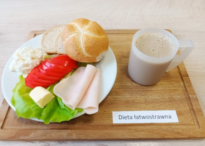 Śniadanie w diecie łatwostrawnej: bułka i kromki białego pieczywa, wędlina drobiowa, twaróg, masło, sałata i pomidor, obok kubek kawy z mlekiem