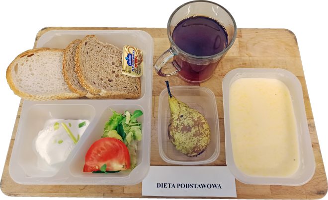 Śniadanie w pojemnikach: pieczywo pszenne i żytnie z porcją masła, twarożek ze szczypiorkiem, sałata z pomidorem, gruszka oraz kubek herbaty. Obok znajduje się kartka z napisem ‘Dieta podstawowa.