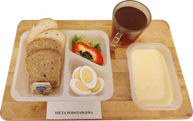 Śniadanie w diecie podstawowej: pieczywo mieszane z masłem, jajko na twardo, sałatka z sałaty i papryki, zupa mleczna oraz herbata, podane na drewnianej desce