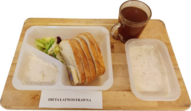 Śniadanie w diecie łatwostrawnej: pieczywo pszenne, pasta twarogowa, masło, sałata, herbata oraz zupa mleczna, podane w pojemnikach na drewnianej desce