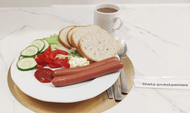 Śniadanie w diecie podstawowej: dwie parówki, kromki białego pieczywa, ogórek, papryka, sałata i ketchup, obok kubek kawy