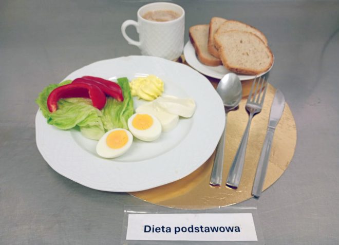 Śniadanie w diecie podstawowej: jajko gotowane, plasterki sera, sałata, papryka i porcja masła, podane z pieczywem oraz kawą
