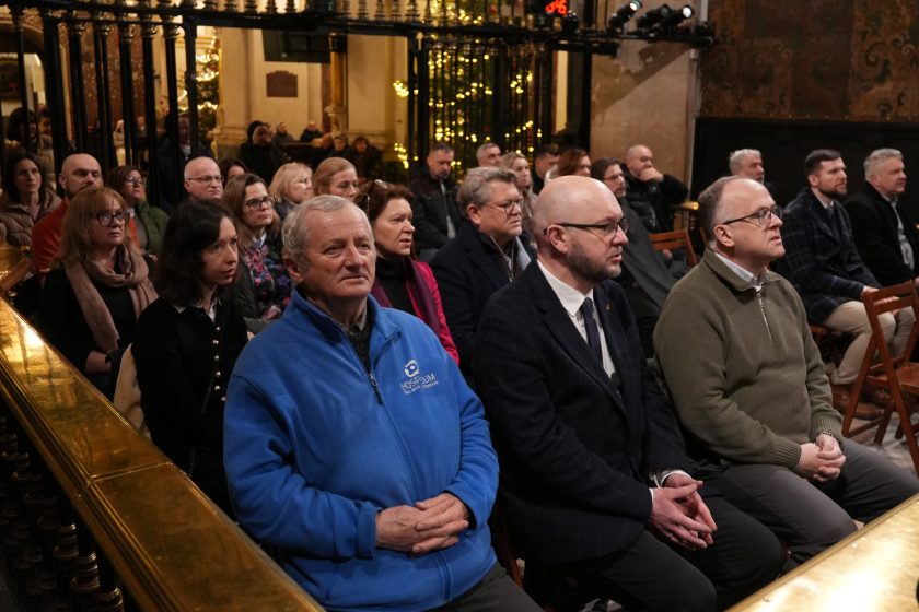Uczestnicy spotkania siedzą w ławkach kaplicy, skupieni i zasłuchani. W pierwszym rzędzie widoczni świeccy współpracownicy oraz osoby duchowne