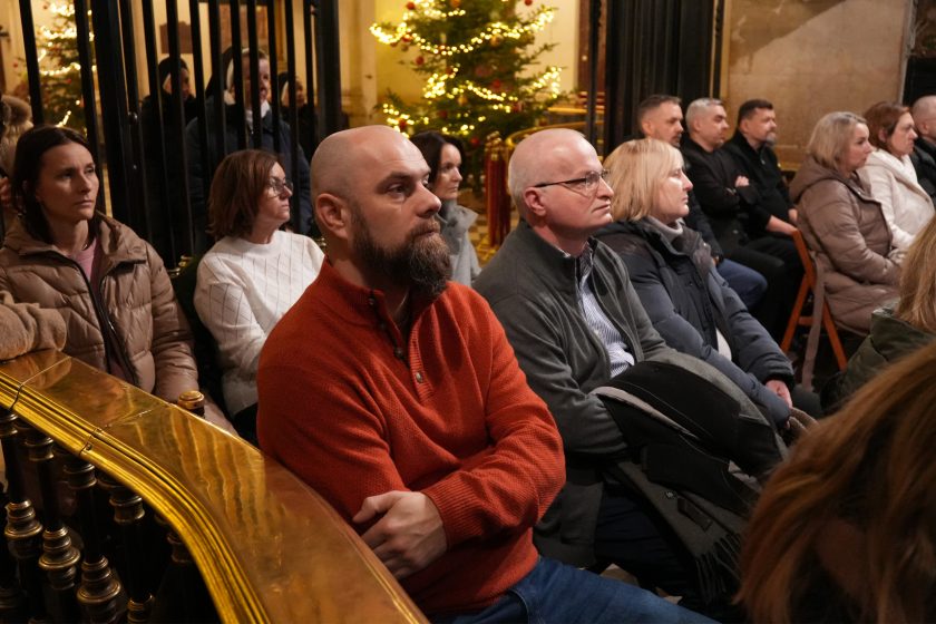 Zgromadzeni świeccy uczestnicy spotkania siedzą w ławkach kaplicy, słuchając liturgii. W tle widoczna świąteczna dekoracja z choinką