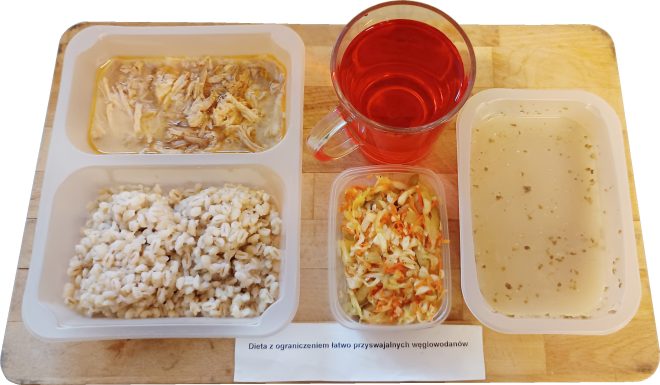 Obiad w diecie z ograniczeniem łatwo przyswajalnych węglowodanów: filet z kurczaka w jasnym sosie, kasza jęczmienna, surówka z kapusty i marchewki, klarowna zupa jarzynowa oraz herbata owocowa, podane na drewnianej tacy