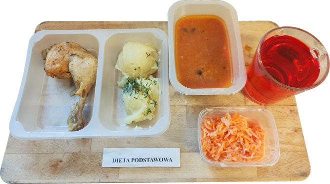 Obiad na diecie podstawowej: pieczona ćwiartka kurczaka, ziemniaki z koperkiem, zupa pomidorowa, surówka z marchewki oraz herbata owocowa, podane w pojemnikach cateringowych na drewnianej desce