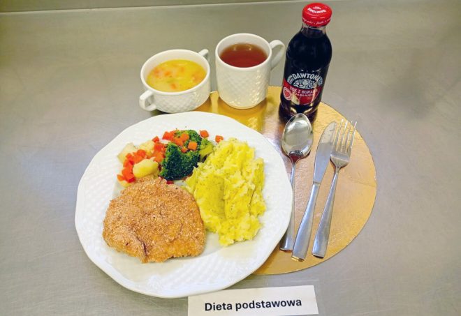Obiad w diecie podstawowej: panierowany kotlet drobiowy, ziemniaki puree, warzywa gotowane, zupa jarzynowa oraz sok owocowy. Obok w butelce widać sok z buraka i jabłek.