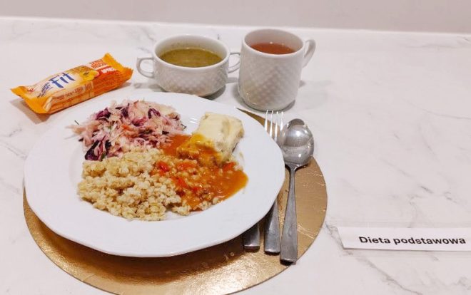 Obiad w diecie podstawowej: ryba gotowana z sosem, kasza pęczak, mieszanka warzyw gotowanych, zupa oraz herbata. Obok widać ciasteczka FIT