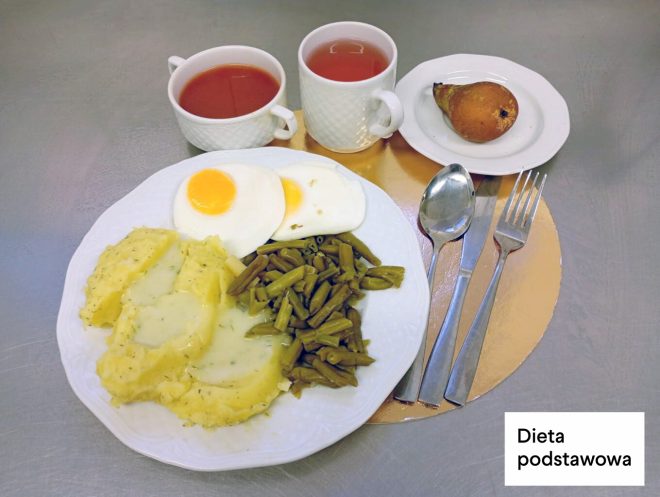 Obiad na diecie podstawowej: ziemniaki z sosem koperkowym, jajka sadzone, fasolka szparagowa, kompot oraz herbata, podane na białym talerzu i tacy