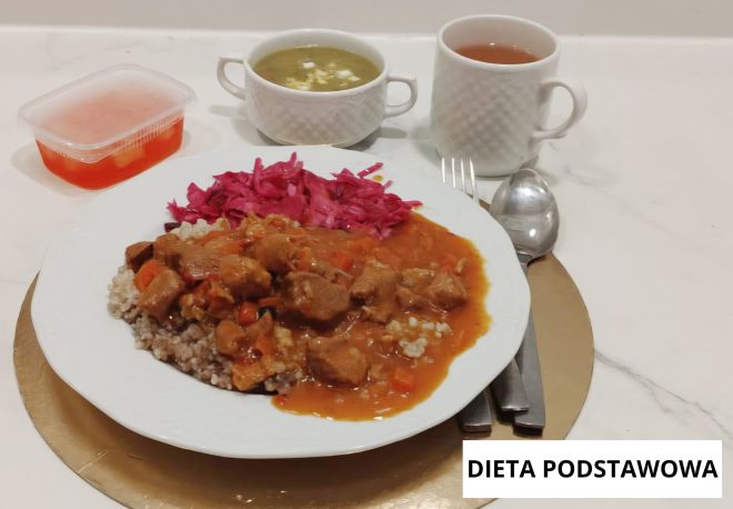 Obiad w diecie podstawowej: gulasz mięsny w sosie pomidorowym podany z kaszą gryczaną oraz surówką z czerwonej kapusty. Obok talerza zupa jarzynowa, kompot oraz herbata. Na zdjęciu widoczny napis „Dieta podstawowa”