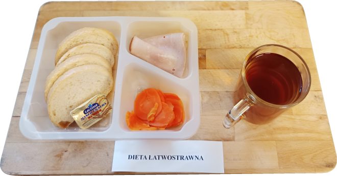 Śniadanie w diecie lekkostrawnej: kromki jasnego pieczywa z masłem, plaster wędliny drobiowej, gotowana marchewka w plastrach oraz herbata, podane na drewnianej tacy