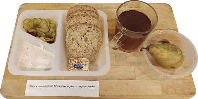 Śniadanie w diecie z ograniczeniem łatwo przyswajalnych węglowodanów: pieczywo razowe, twarożek z ziołami, ogórek kiszony, masło, herbata oraz gruszka, podane na tacy