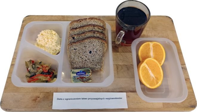 Śniadanie w diecie z ograniczeniem łatwo przyswajalnych węglowodanów: kromki chleba pełnoziarnistego z masłem, twarożek, sałatka warzywna, herbata oraz połówki pomarańczy, podane na tacy