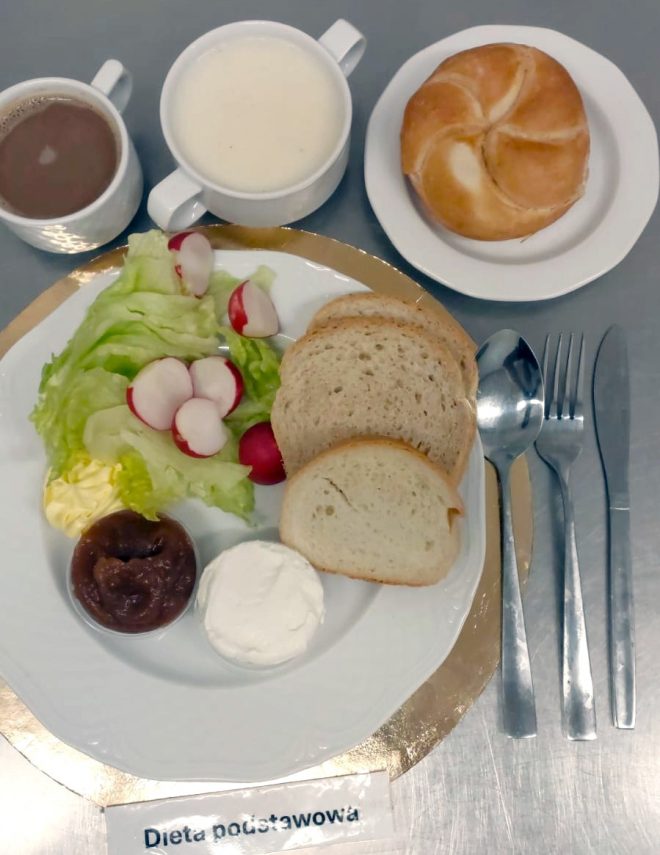 Śniadanie w diecie podstawowej: pieczywo pszenne, twaróg, sałata z rzodkiewką, porcja masła i dżemu. Do posiłku podano kawę, mleko oraz bułkę pszenną