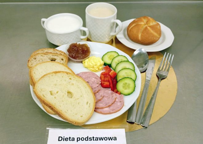 Śniadanie w diecie podstawowej: pieczywo pszenne, plasterki wędliny, świeże warzywa – ogórek i papryka – masło oraz dżem. Do posiłku podano kawę, mleko i bułkę